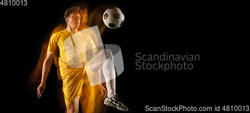 Image of Young caucasian male football or soccer player kicking ball for the goal in mixed light on dark background. Concept of healthy lifestyle, professional sport, hobby.