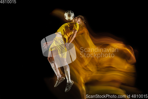 Image of Young caucasian male football or soccer player kicking ball for the goal in mixed light on dark background. Concept of healthy lifestyle, professional sport, hobby.