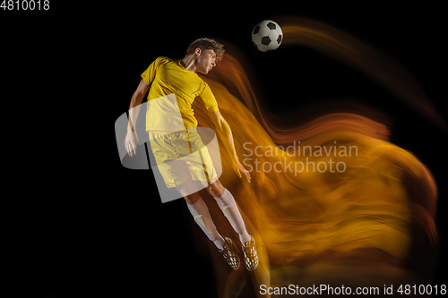 Image of Young caucasian male football or soccer player kicking ball for the goal in mixed light on dark background. Concept of healthy lifestyle, professional sport, hobby.