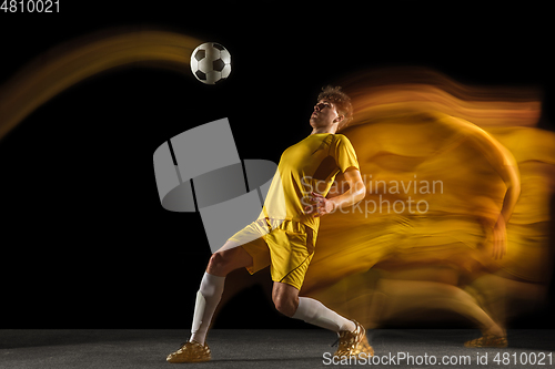 Image of Young caucasian male football or soccer player kicking ball for the goal in mixed light on dark background. Concept of healthy lifestyle, professional sport, hobby.