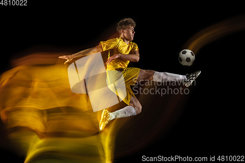 Image of Young caucasian male football or soccer player kicking ball for the goal in mixed light on dark background. Concept of healthy lifestyle, professional sport, hobby.