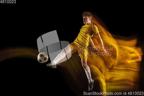 Image of Young caucasian male football or soccer player kicking ball for the goal in mixed light on dark background. Concept of healthy lifestyle, professional sport, hobby.