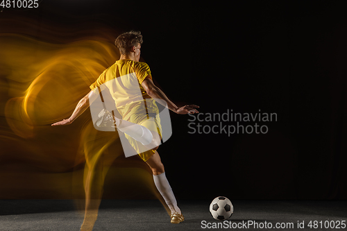 Image of Young caucasian male football or soccer player kicking ball for the goal in mixed light on dark background. Concept of healthy lifestyle, professional sport, hobby.