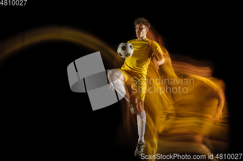 Image of Young caucasian male football or soccer player kicking ball for the goal in mixed light on dark background. Concept of healthy lifestyle, professional sport, hobby.