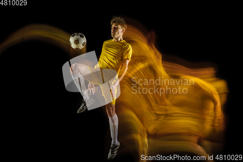 Image of Young caucasian male football or soccer player kicking ball for the goal in mixed light on dark background. Concept of healthy lifestyle, professional sport, hobby.