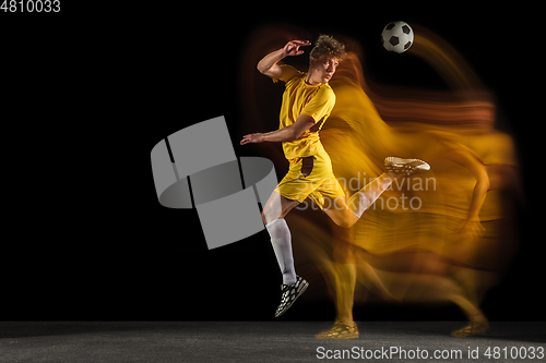 Image of Young caucasian male football or soccer player kicking ball for the goal in mixed light on dark background. Concept of healthy lifestyle, professional sport, hobby.