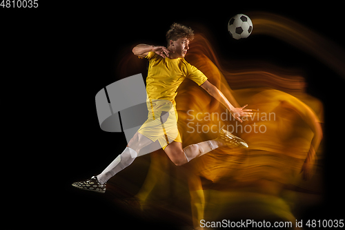 Image of Young caucasian male football or soccer player kicking ball for the goal in mixed light on dark background. Concept of healthy lifestyle, professional sport, hobby.