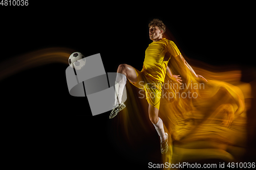 Image of Young caucasian male football or soccer player kicking ball for the goal in mixed light on dark background. Concept of healthy lifestyle, professional sport, hobby.