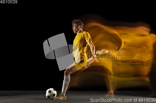 Image of Young caucasian male football or soccer player kicking ball for the goal in mixed light on dark background. Concept of healthy lifestyle, professional sport, hobby.