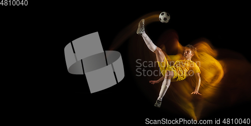 Image of Young caucasian male football or soccer player kicking ball for the goal in mixed light on dark background. Concept of healthy lifestyle, professional sport, hobby.