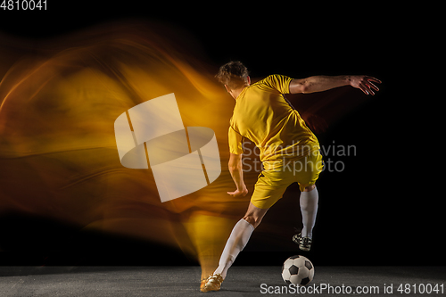 Image of Young caucasian male football or soccer player kicking ball for the goal in mixed light on dark background. Concept of healthy lifestyle, professional sport, hobby.