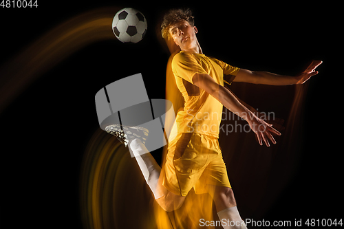 Image of Young caucasian male football or soccer player kicking ball for the goal in mixed light on dark background. Concept of healthy lifestyle, professional sport, hobby.