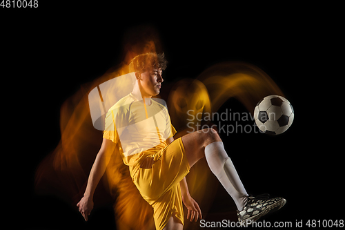 Image of Young caucasian male football or soccer player kicking ball for the goal in mixed light on dark background. Concept of healthy lifestyle, professional sport, hobby.