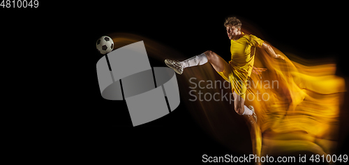 Image of Young caucasian male football or soccer player kicking ball for the goal in mixed light on dark background. Concept of healthy lifestyle, professional sport, hobby.