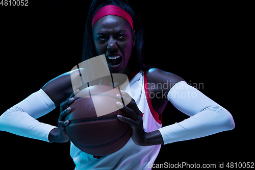 Image of Beautiful african-american female basketball player in motion and action in neon light on black background. Concept of healthy lifestyle, professional sport, hobby.