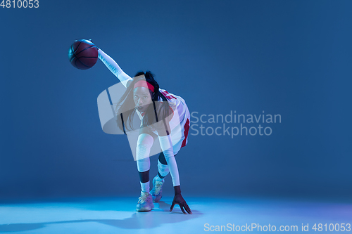 Image of Beautiful african-american female basketball player in motion and action in neon light on blue background. Concept of healthy lifestyle, professional sport, hobby.