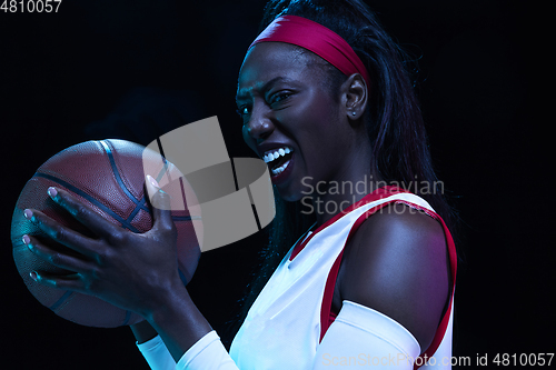 Image of Beautiful african-american female basketball player in motion and action in neon light on black background. Concept of healthy lifestyle, professional sport, hobby.
