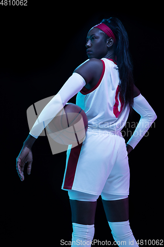 Image of Beautiful african-american female basketball player in motion and action in neon light on black background. Concept of healthy lifestyle, professional sport, hobby.