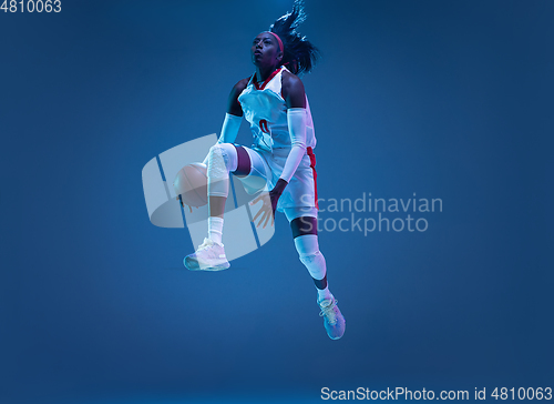 Image of Beautiful african-american female basketball player in motion and action in neon light on blue background. Concept of healthy lifestyle, professional sport, hobby.