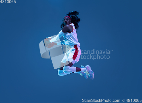 Image of Beautiful african-american female basketball player in motion and action in neon light on blue background. Concept of healthy lifestyle, professional sport, hobby.