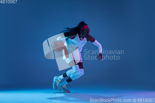 Image of Beautiful african-american female basketball player in motion and action in neon light on blue background. Concept of healthy lifestyle, professional sport, hobby.