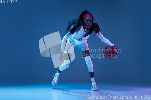 Image of Beautiful african-american female basketball player in motion and action in neon light on blue background. Concept of healthy lifestyle, professional sport, hobby.