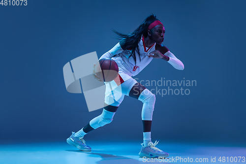 Image of Beautiful african-american female basketball player in motion and action in neon light on blue background. Concept of healthy lifestyle, professional sport, hobby.