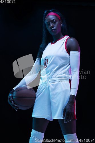 Image of Beautiful african-american female basketball player in motion and action in neon light on black background. Concept of healthy lifestyle, professional sport, hobby.