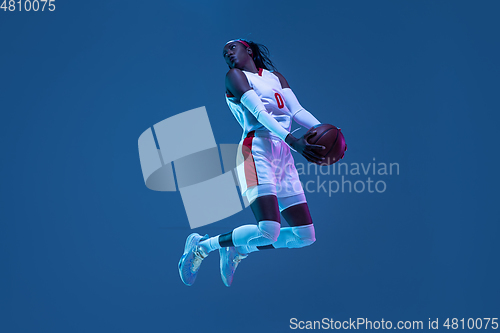 Image of Beautiful african-american female basketball player in motion and action in neon light on blue background. Concept of healthy lifestyle, professional sport, hobby.