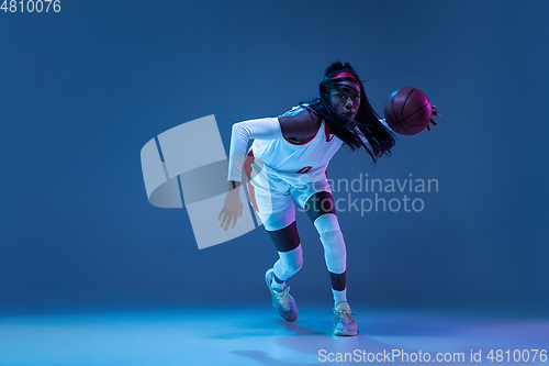 Image of Beautiful african-american female basketball player in motion and action in neon light on blue background. Concept of healthy lifestyle, professional sport, hobby.