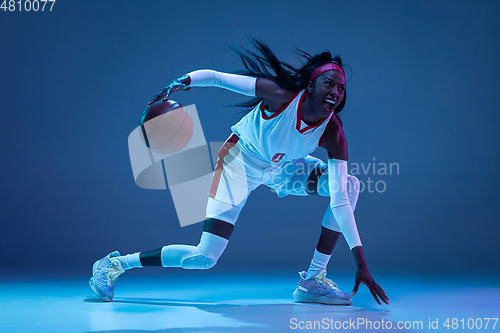 Image of Beautiful african-american female basketball player in motion and action in neon light on blue background. Concept of healthy lifestyle, professional sport, hobby.