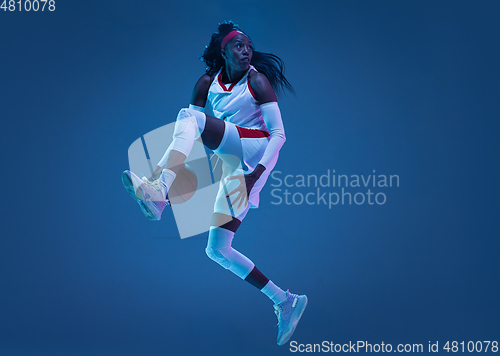 Image of Beautiful african-american female basketball player in motion and action in neon light on blue background. Concept of healthy lifestyle, professional sport, hobby.