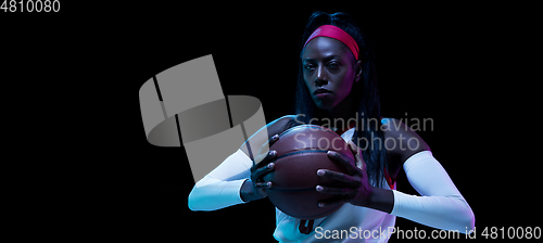 Image of Beautiful african-american female basketball player in motion and action in neon light on black background. Concept of healthy lifestyle, professional sport, hobby.