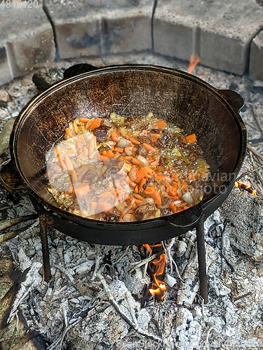 Image of gourmet beef stew cooked in cauldron on outdoor fire pit