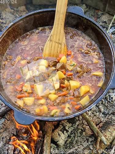 Image of gourmet beef stew cooked in cauldron on outdoor fire pit