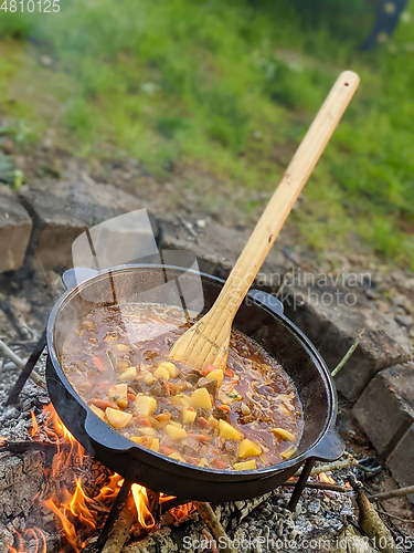 Image of gourmet beef stew cooked in cauldron on outdoor fire pit