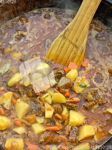 Image of gourmet beef stew cooked in cauldron on outdoor fire pit