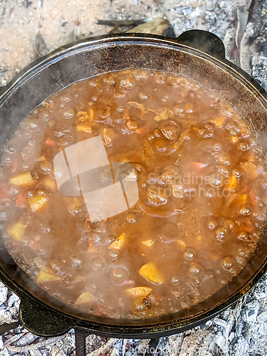 Image of gourmet beef stew cooked in cauldron on outdoor fire pit