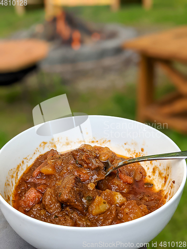 Image of gourmet beef stew cooked in cauldron on outdoor fire pit