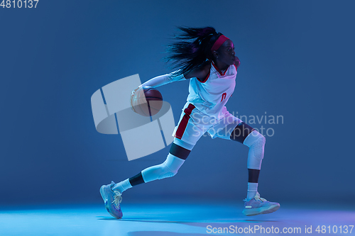 Image of Beautiful african-american female basketball player in motion and action in neon light on blue background. Concept of healthy lifestyle, professional sport, hobby.