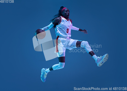 Image of Beautiful african-american female basketball player in motion and action in neon light on blue background. Concept of healthy lifestyle, professional sport, hobby.