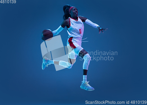 Image of Beautiful african-american female basketball player in motion and action in neon light on blue background. Concept of healthy lifestyle, professional sport, hobby.