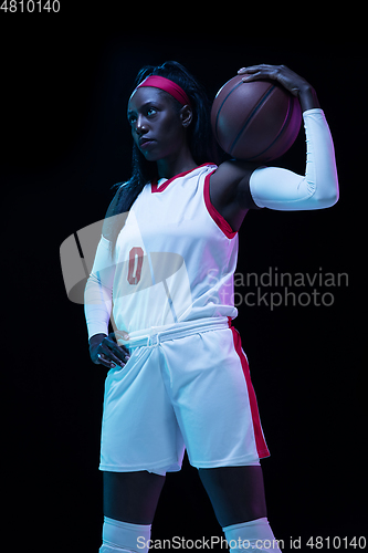 Image of Beautiful african-american female basketball player in motion and action in neon light on black background. Concept of healthy lifestyle, professional sport, hobby.