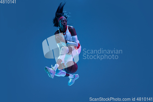 Image of Beautiful african-american female basketball player in motion and action in neon light on blue background. Concept of healthy lifestyle, professional sport, hobby.