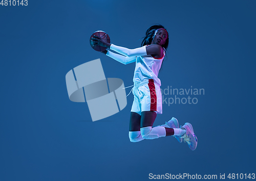 Image of Beautiful african-american female basketball player in motion and action in neon light on blue background. Concept of healthy lifestyle, professional sport, hobby.