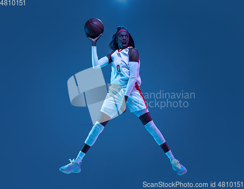 Image of Beautiful african-american female basketball player in motion and action in neon light on blue background. Concept of healthy lifestyle, professional sport, hobby.