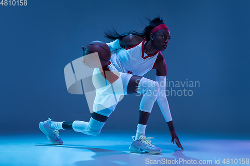 Image of Beautiful african-american female basketball player in motion and action in neon light on blue background. Concept of healthy lifestyle, professional sport, hobby.