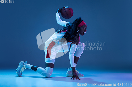 Image of Beautiful african-american female basketball player in motion and action in neon light on blue background. Concept of healthy lifestyle, professional sport, hobby.