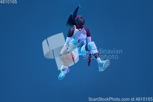 Image of Beautiful african-american female basketball player in motion and action in neon light on blue background. Concept of healthy lifestyle, professional sport, hobby.