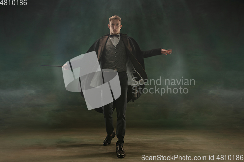 Image of Young man in art action isolated on dark green background. Retro style, comparison of eras concept.